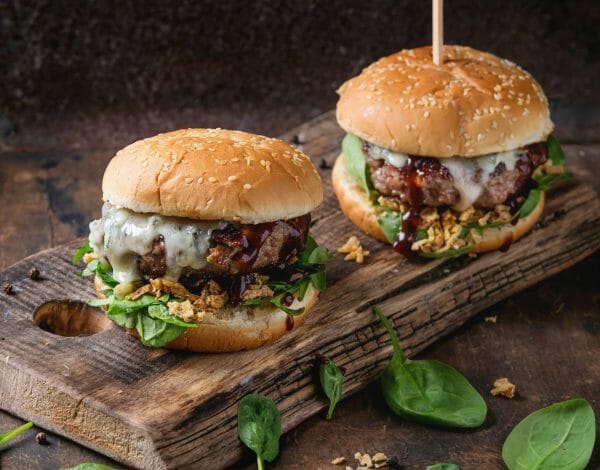 Two gourmet cheeseburgers with spinach, onions, and BBQ sauce.