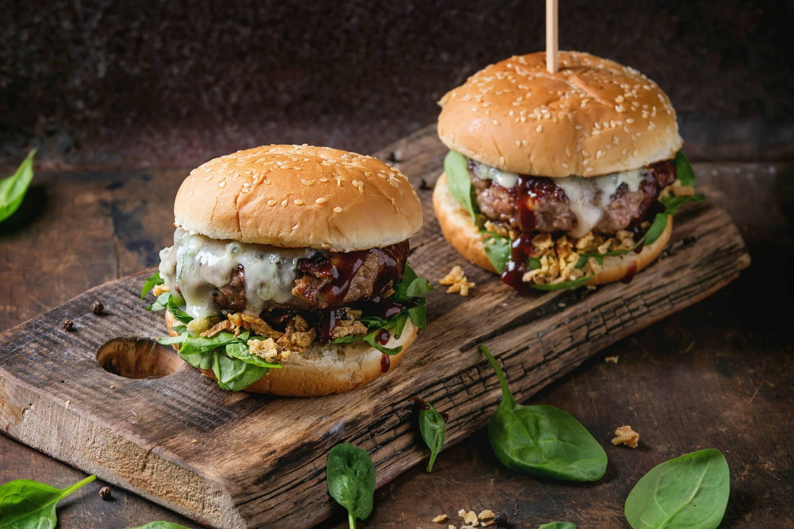 Two gourmet cheeseburgers with spinach, onions, and BBQ sauce.
